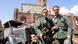 Film still from "Our mothers, Our Fathers" showing two young soldiers pose in front of ruins