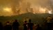 Fire, smoke visible over forested hills, people in foreground watching